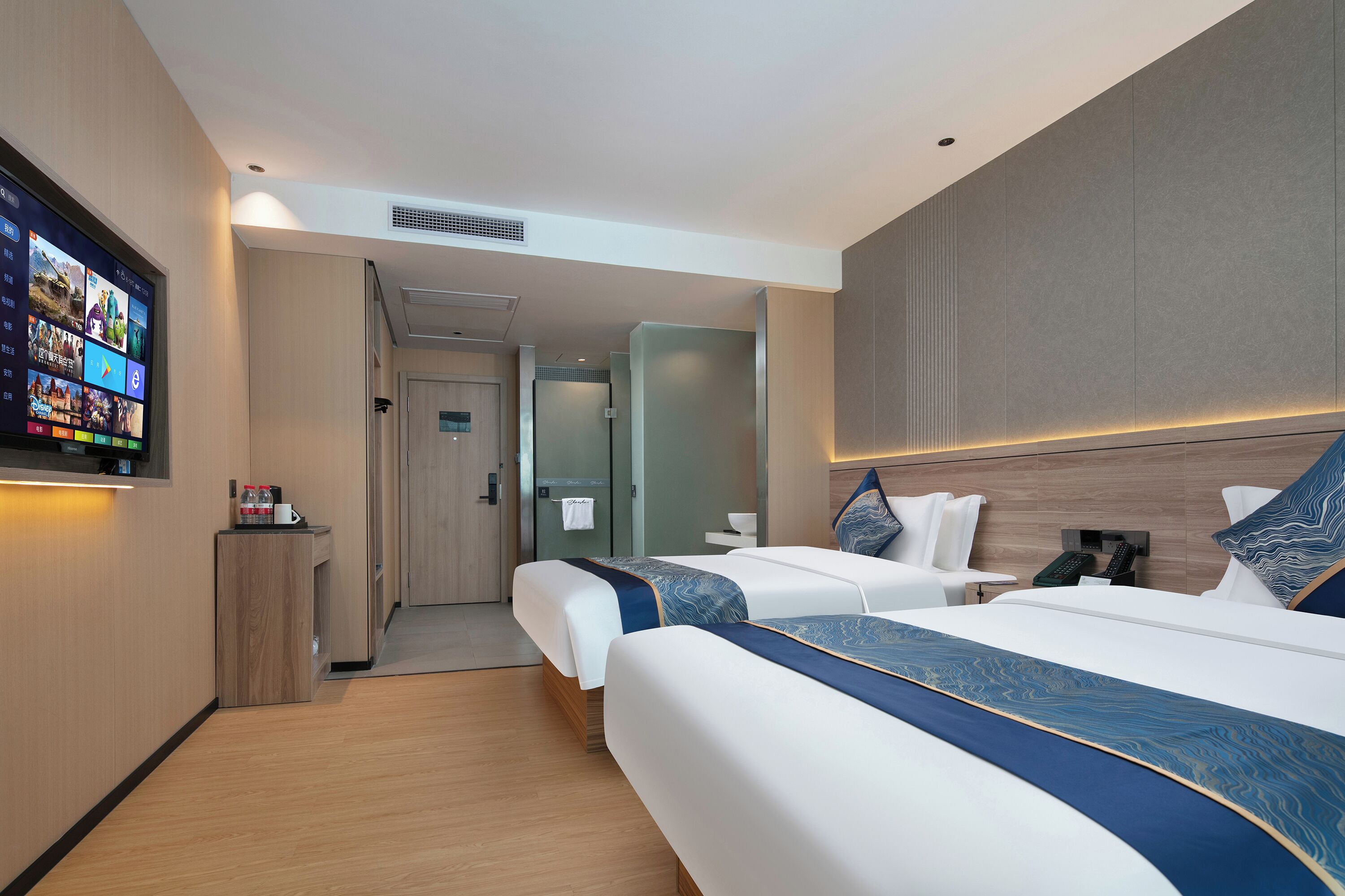 A hotel room with two beds, a TV, a small table with a bottle, and a wall-mounted phone.