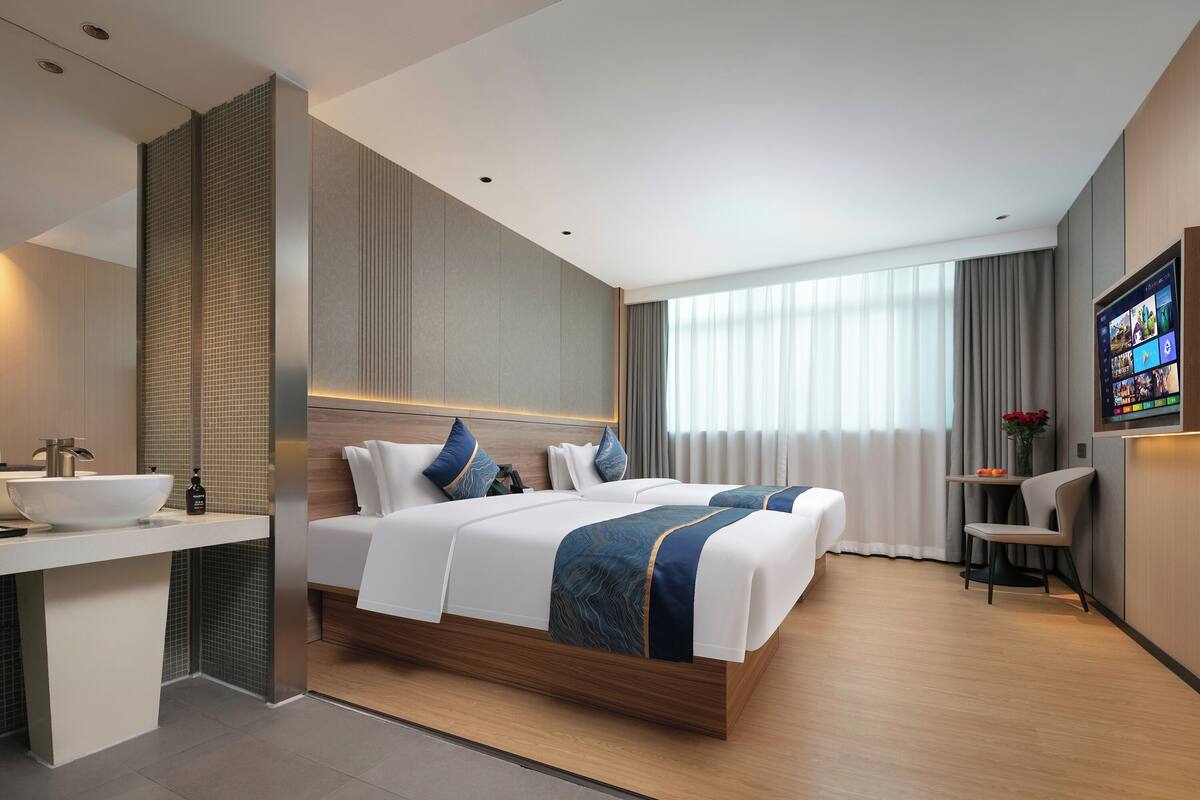 A modern hotel room with a large bed, a bedside table, a built-in sink, and a TV on the wall.