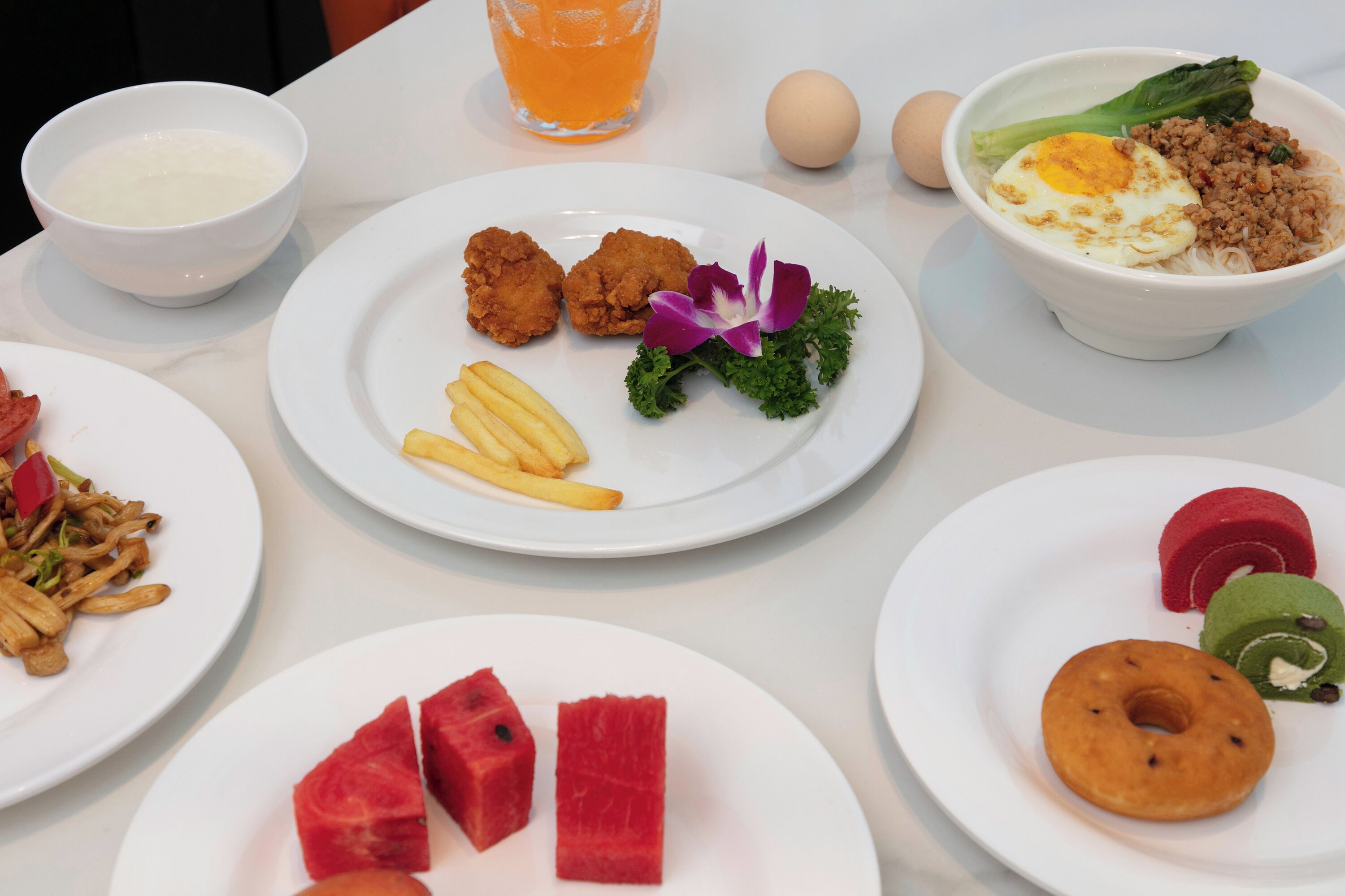 A table with various dishes including fried chicken, French fries, and a bowl of noodles with vegetables.
