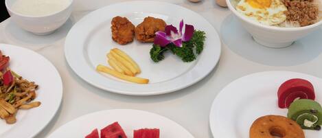 A table with various dishes including fried chicken, French fries, and a bowl of noodles with vegetables.