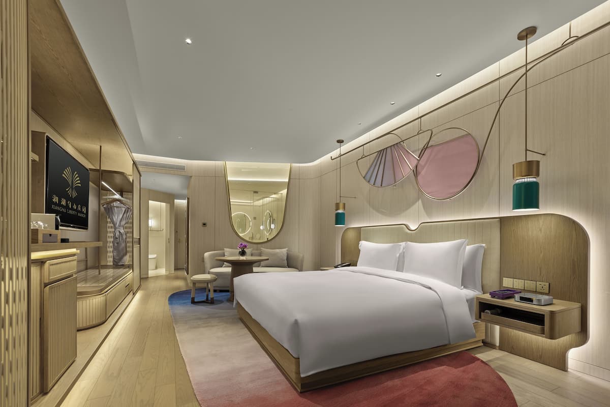 Una habitación de hotel moderna con una cama grande, un tocador con espejo y un televisor en la pared.
