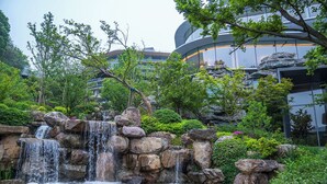 A waterfall surrounded by rocks and greenery, with modern buildings in the background. - Xianghu Liberty Manor (Hangzhou)