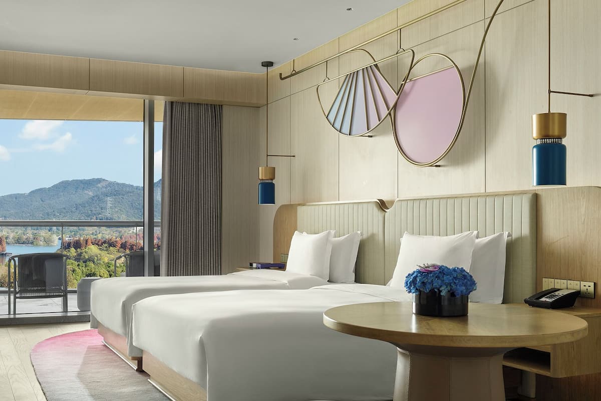 Habitación de hotel con dos camas, una mesa redonda y vistas al exterior.