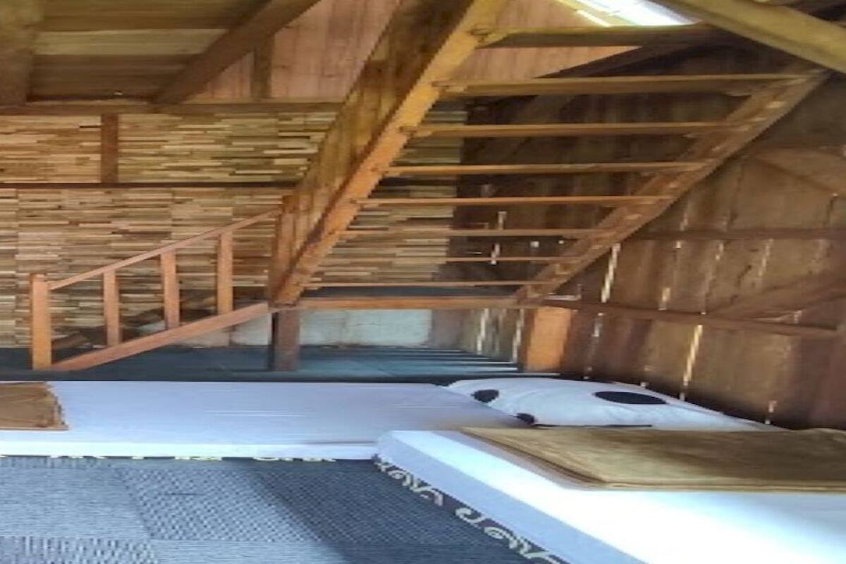 A rustic wooden room with a sloped ceiling, a staircase, and a checkered floor.