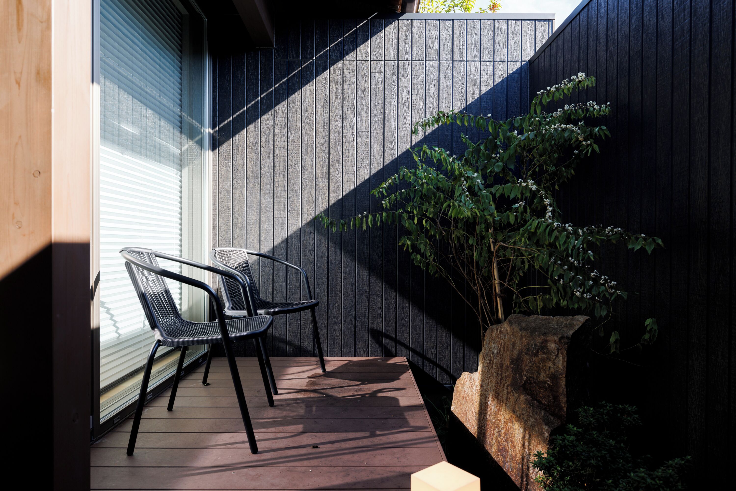 A patio with two chairs, a large rock planter, and a wooden deck.
