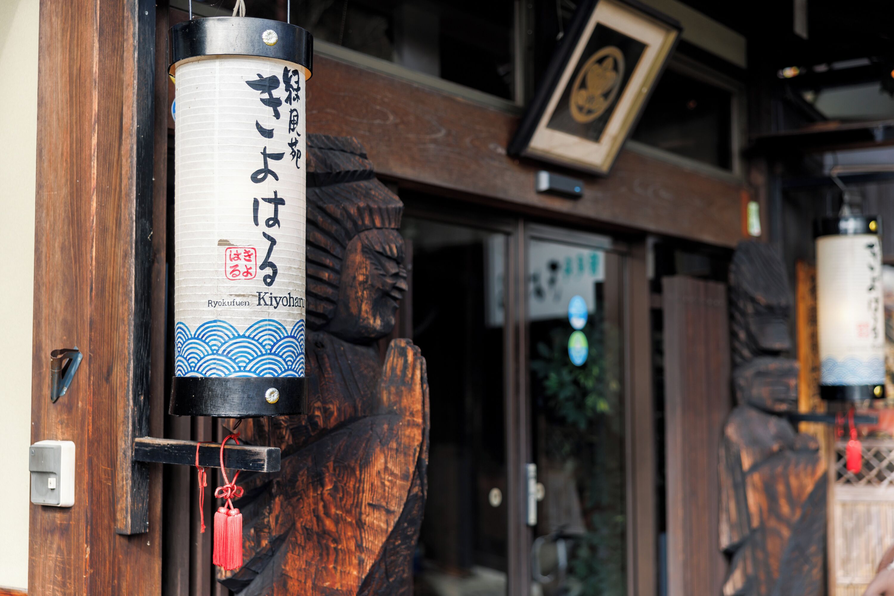 A traditional Japanese building entrance with wooden carvings and a hanging sign with Japanese characters.
