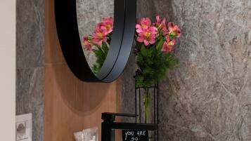 Un bagno con un lavandino bianco, uno specchio nero e fiori rosa.