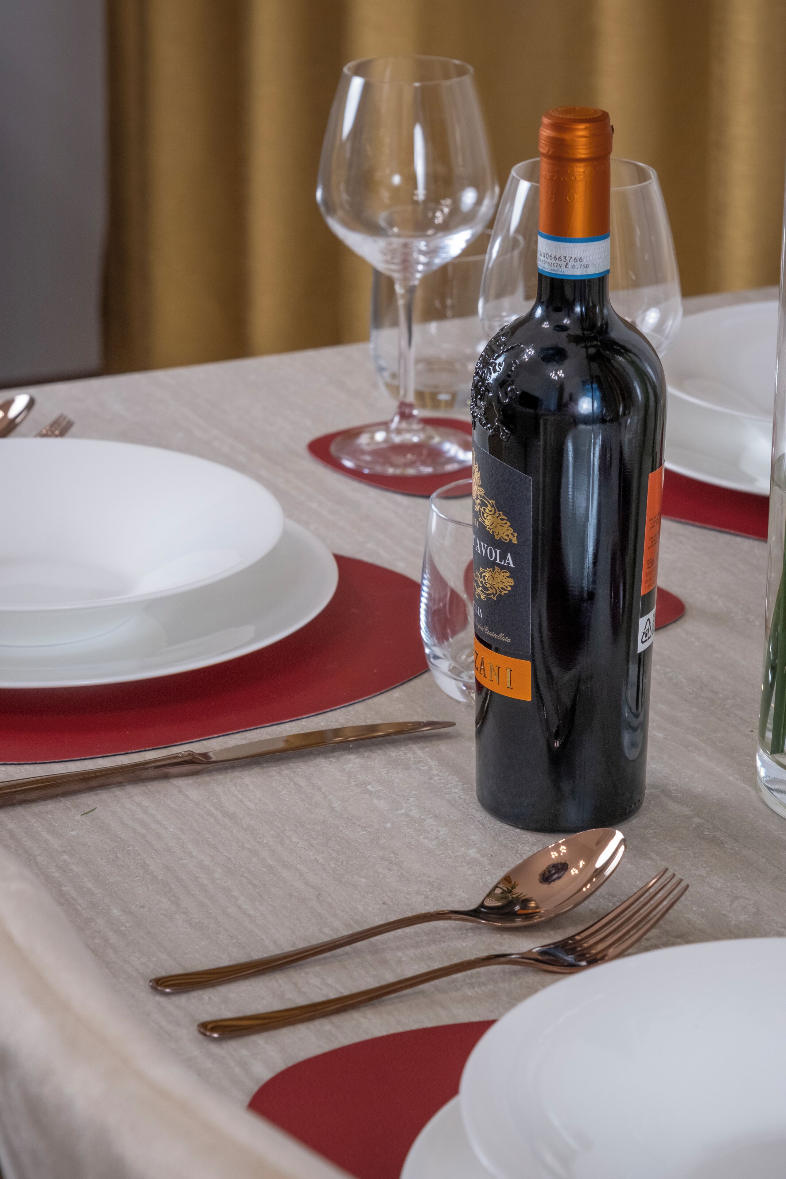 A table set for a meal with a bottle of wine, glasses, and cutlery.
