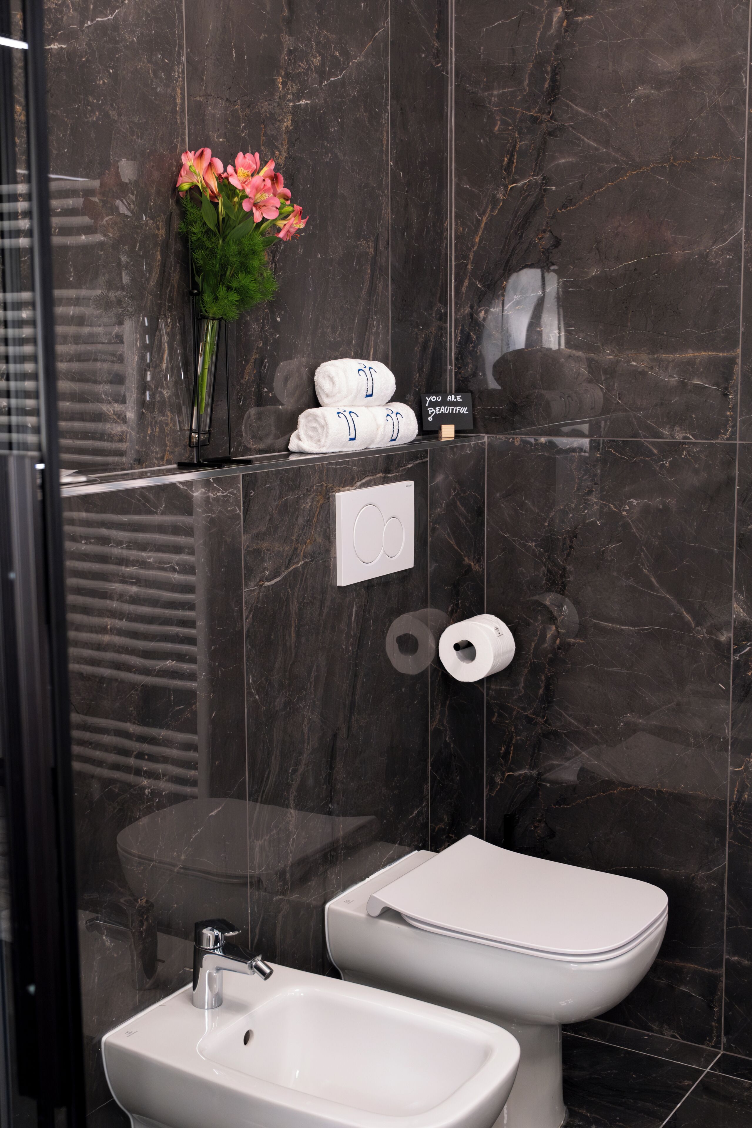 Une salle de bain moderne avec un pare-baignoire en marbre, des toilettes, un bidet et un lavabo.