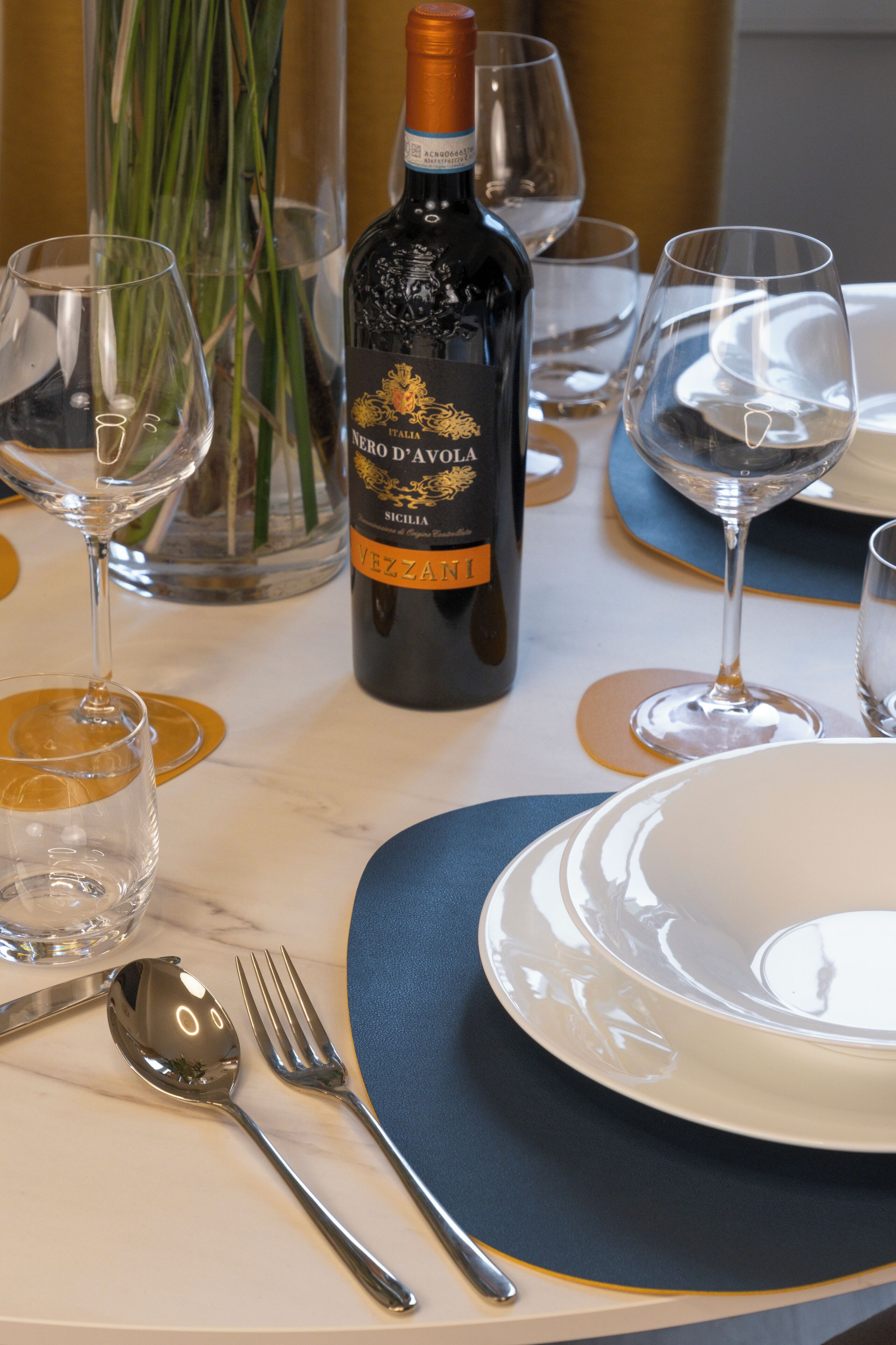 Ein gedeckter Tisch mit einer Flasche Nero d'Avola Wein, klaren Weingenüssen und Besteck.