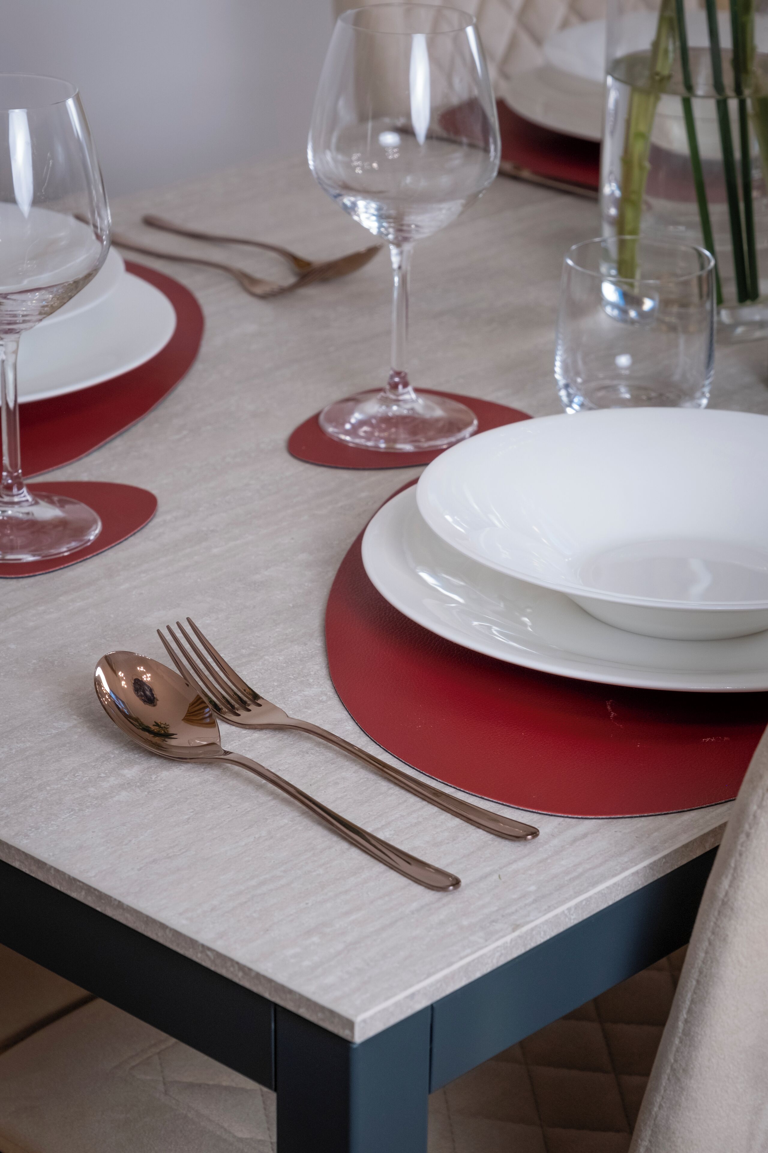 Une table dressée avec de l’assiette blanche, des sets de table rouges et des couverts dorés.