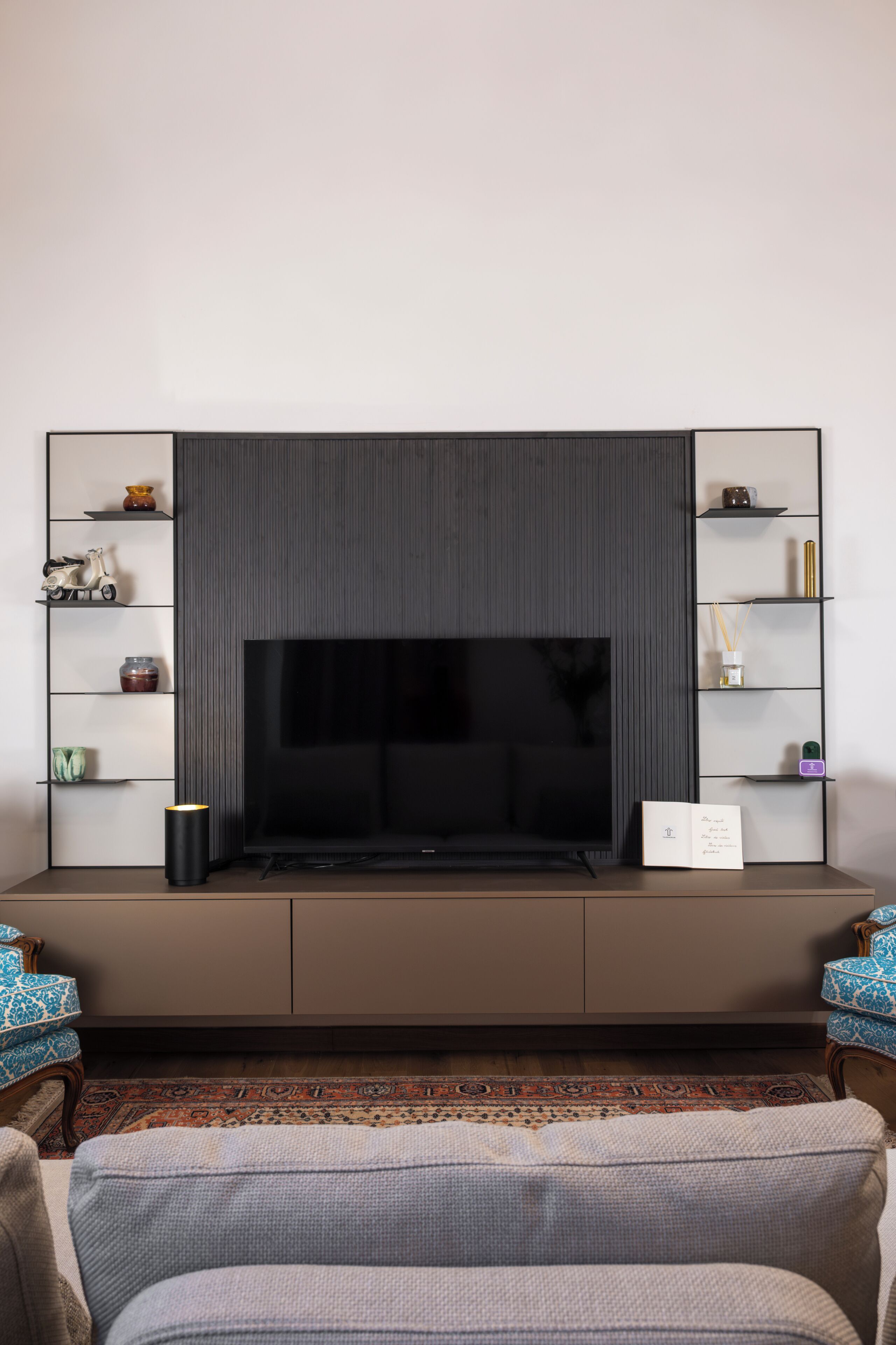 A modern living room with a large flat-screen TV mounted on a dark wall, flanked by white shelving units with various decorative items.
