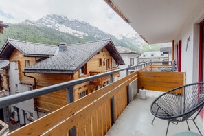 Een balkon met houten hekwerk, een stoel en uitzicht op berghuizen.
