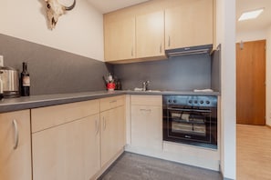 A kitchen with light wooden cabinets, a stainless steel stove, and a wine bottle on the counter.