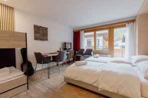 A hotel room with a bed, a desk, two chairs, a television, and a view of the outside.