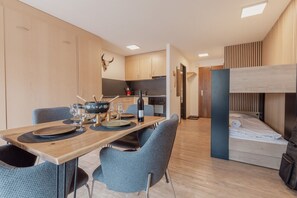 A compact hotel room with a bunk bed, a dining area with a table set for two, and a kitchenette. - Charming studio in the center of Saas-Fee (Saas-Fee)
