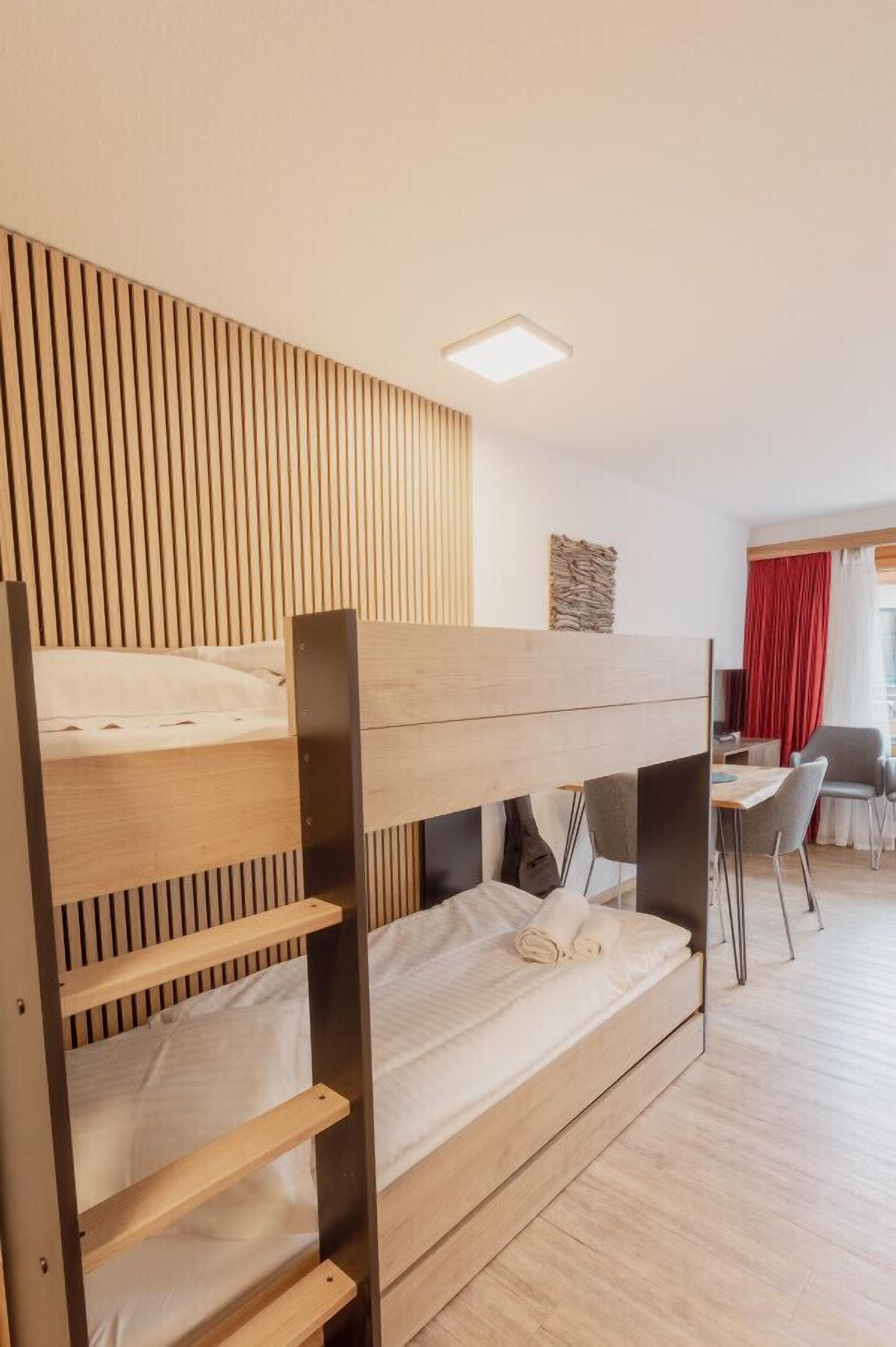 A bunk bed room with a wooden slat wall, a small table, and a chair.