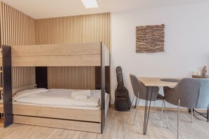 Ein Schlafraum mit Etagenbetten, einer Wand aus Holzslattern, einer Gitarre, einem Schreibtisch und zwei Stühlen.
