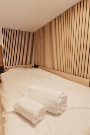 A neatly made bed with a wooden headboard and two rolled towels on it.