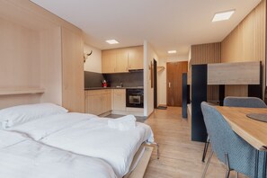 Moderni hotellihuone, jossa on suuri sänky, ruokapöytä ja pieni keittiönurkkaus.