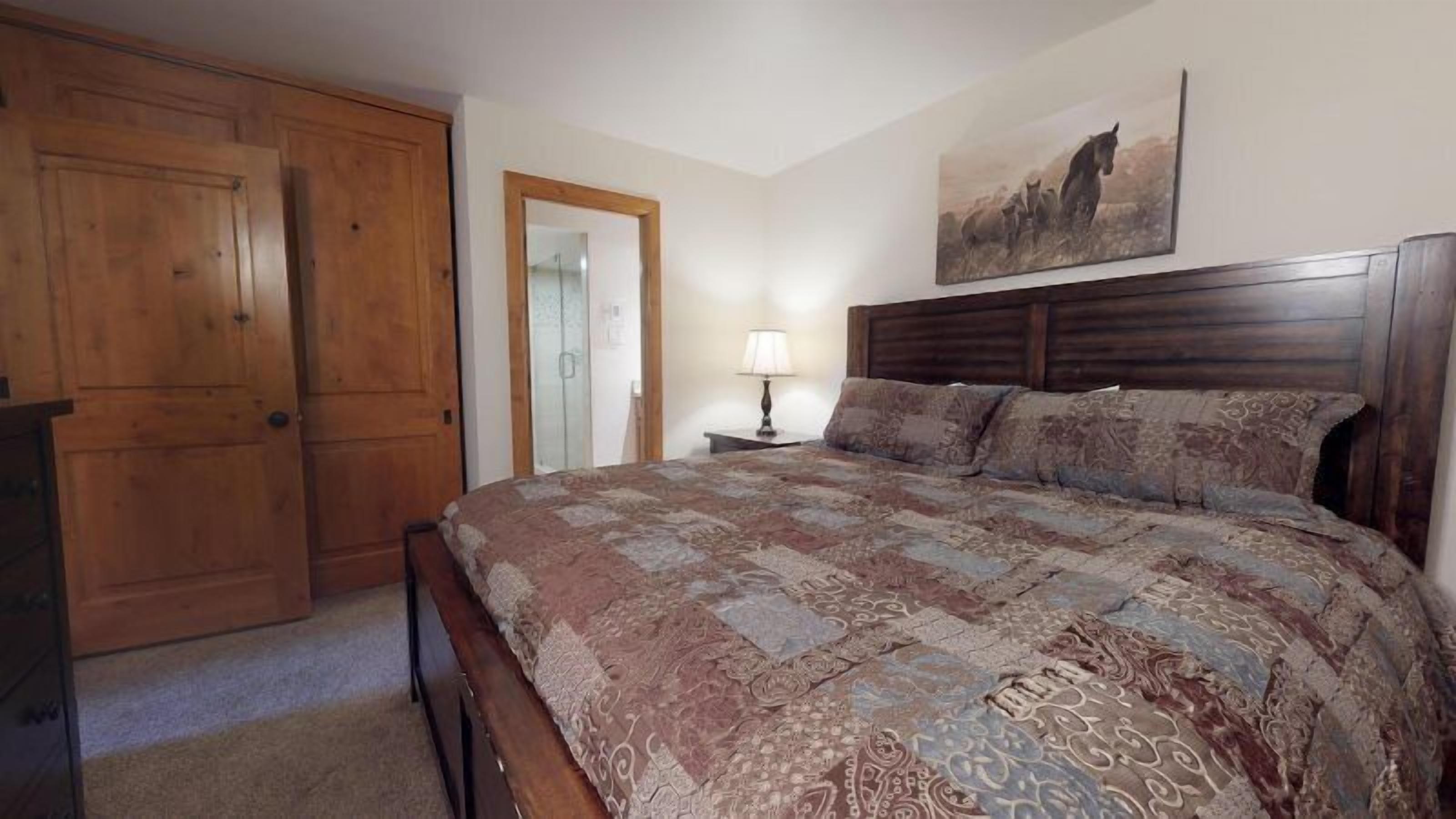 A bedroom with a large bed, wooden wardrobe, and a painting on the wall.