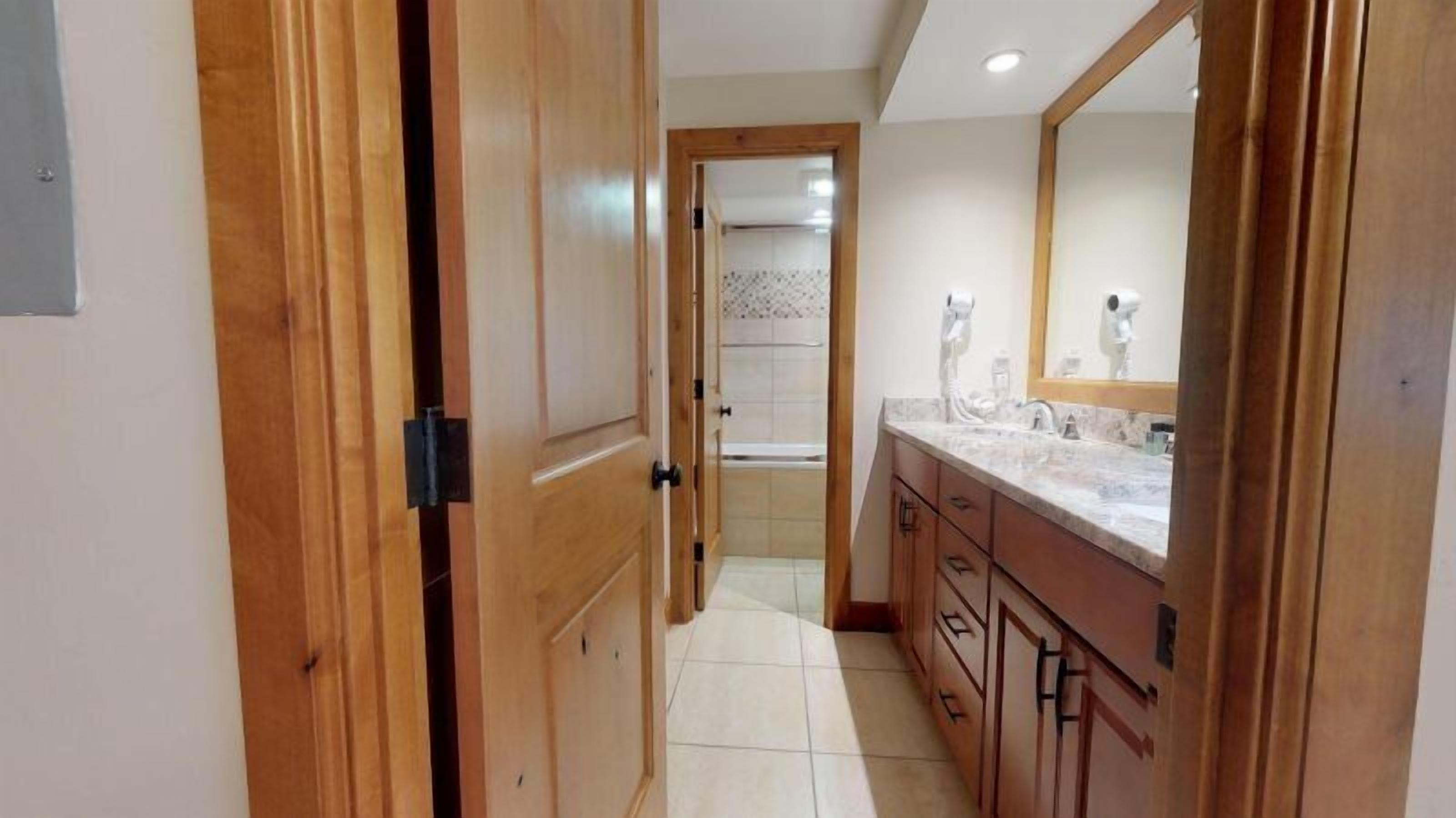 A hallway with wooden doors, a bathroom with a sink and mirror, and a shower area.