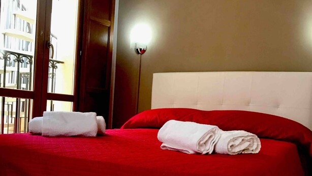 A hotel room with a large bed, red bedding, and two white towels.