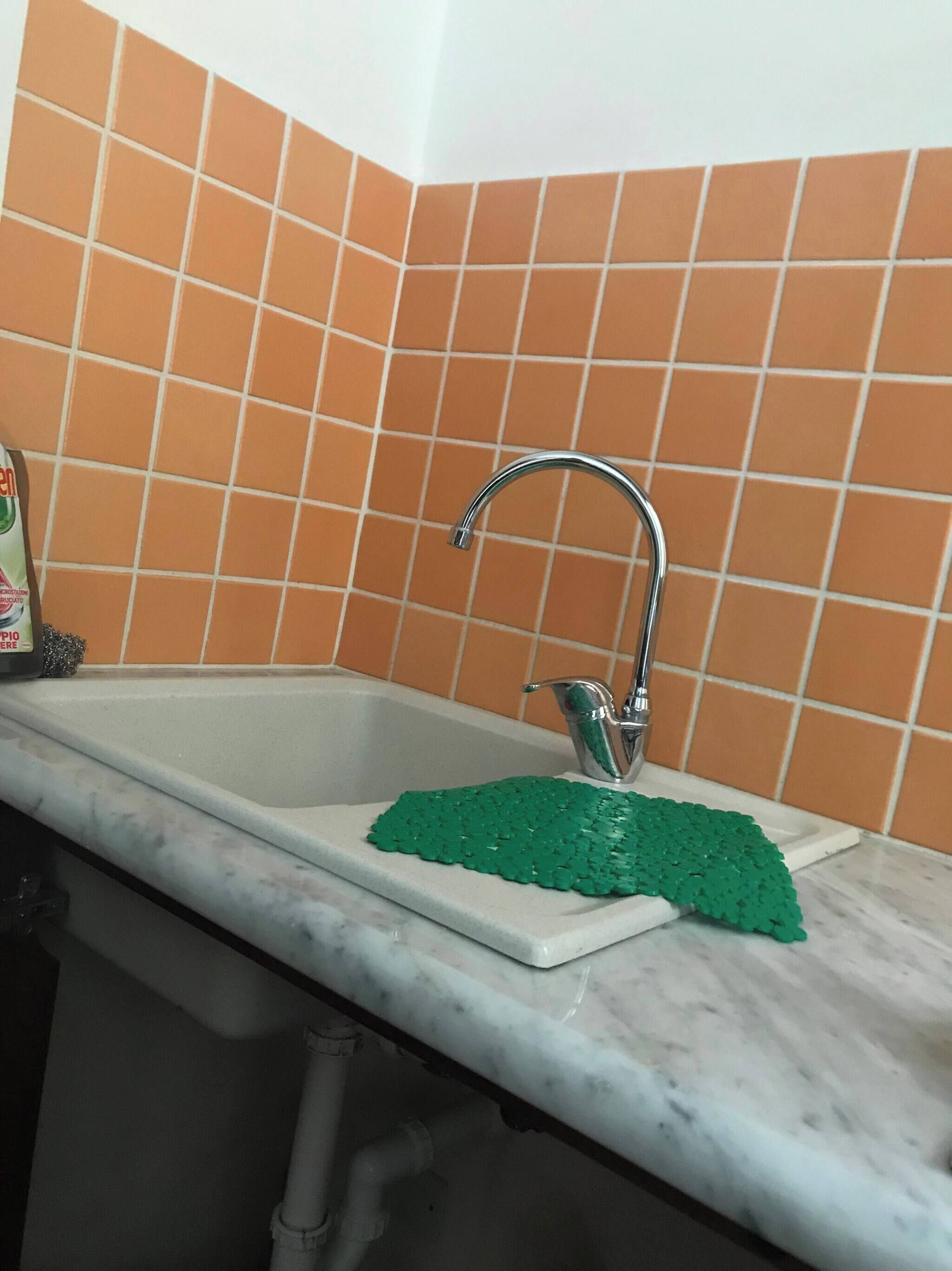 A kitchen sink with a green mat, a faucet, and orange-tiled walls.