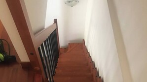A wooden staircase with a handrail, leading to a landing with a white wall and a ceiling light fixture.