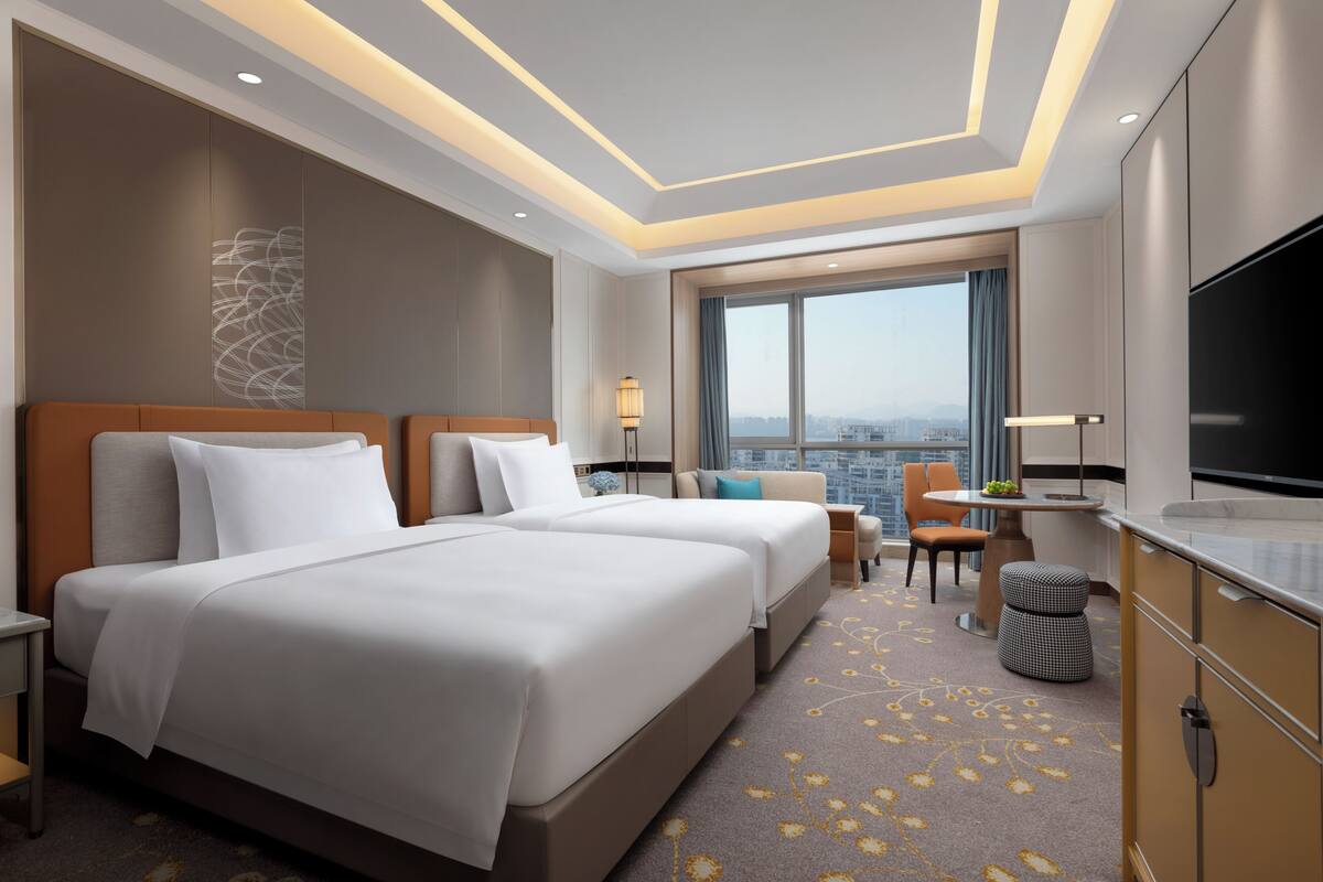 A hotel room with two beds, a TV, a desk with a chair, and a view of the city.