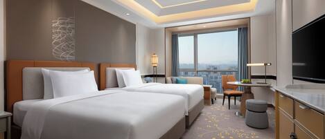 Habitación de hotel con dos camas, televisión, escritorio y vistas a la ciudad.