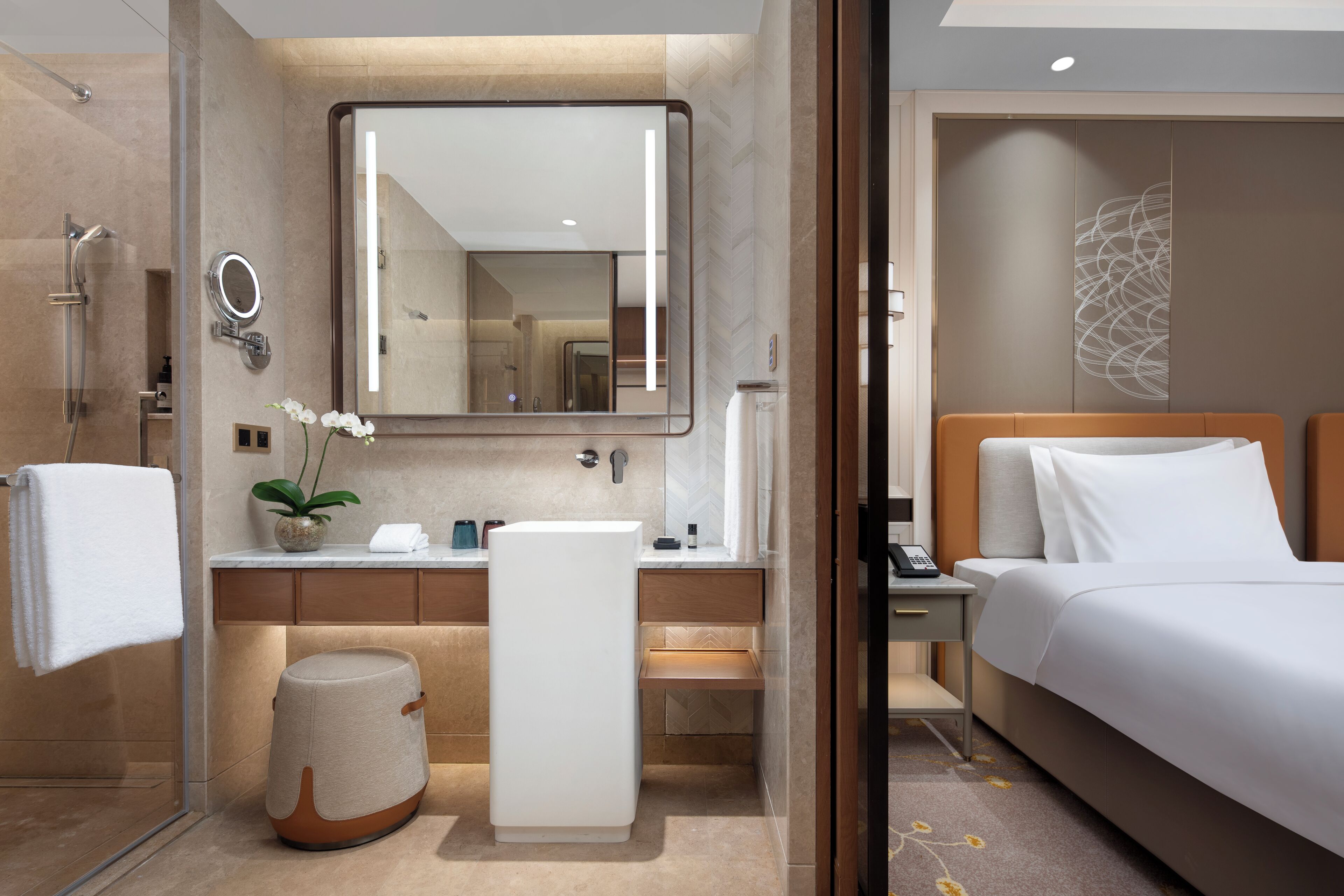A modern hotel room with a large bed, a bedside table, a nightstand, a bathroom with a shower, a sink, and a mirror.