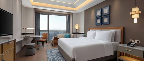 A modern hotel room with a large bed, a desk, a chair, a TV, and a city view.