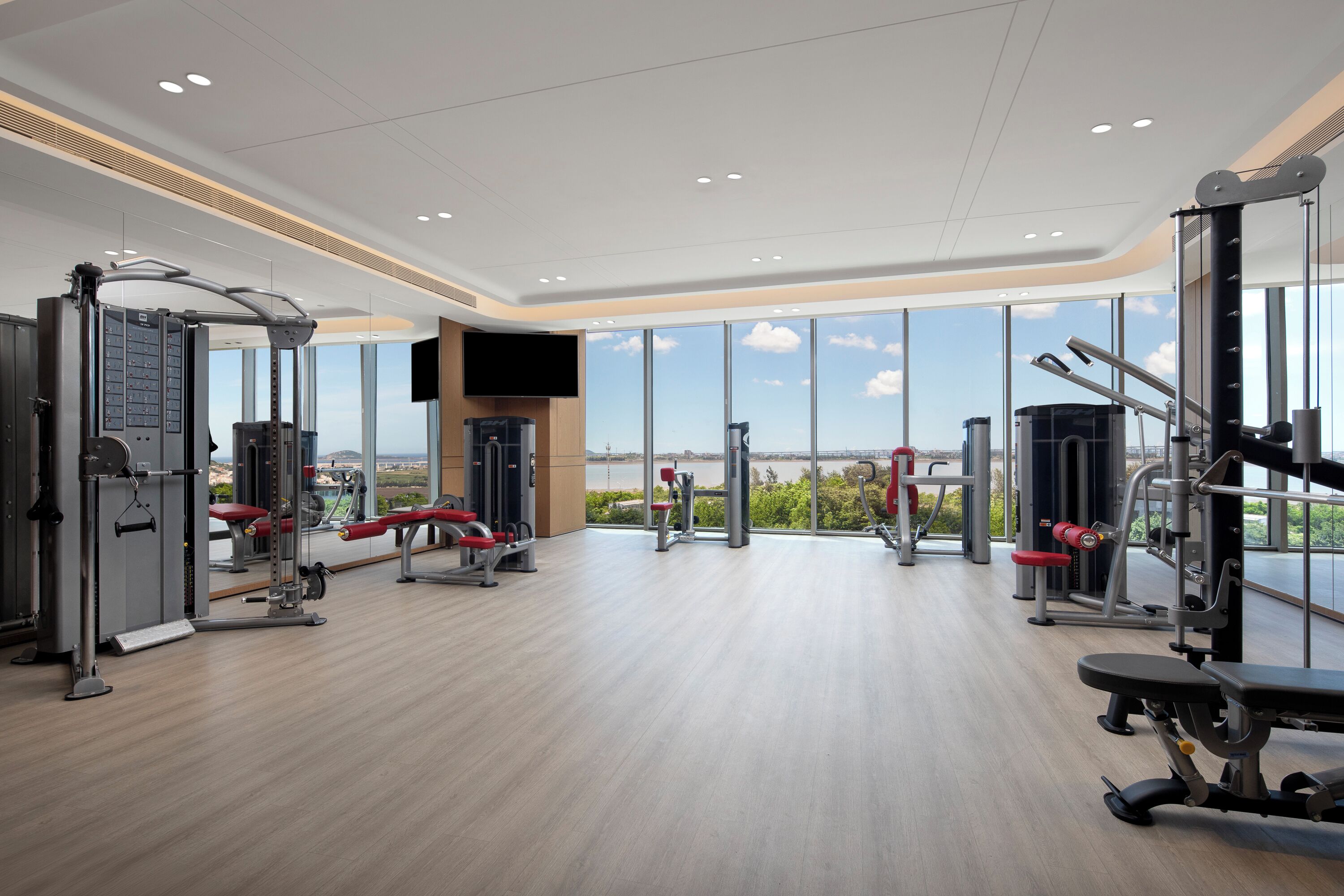 Een moderne sportschool met diverse trainingsapparaten, grote ramen en uitzicht op de omgeving.