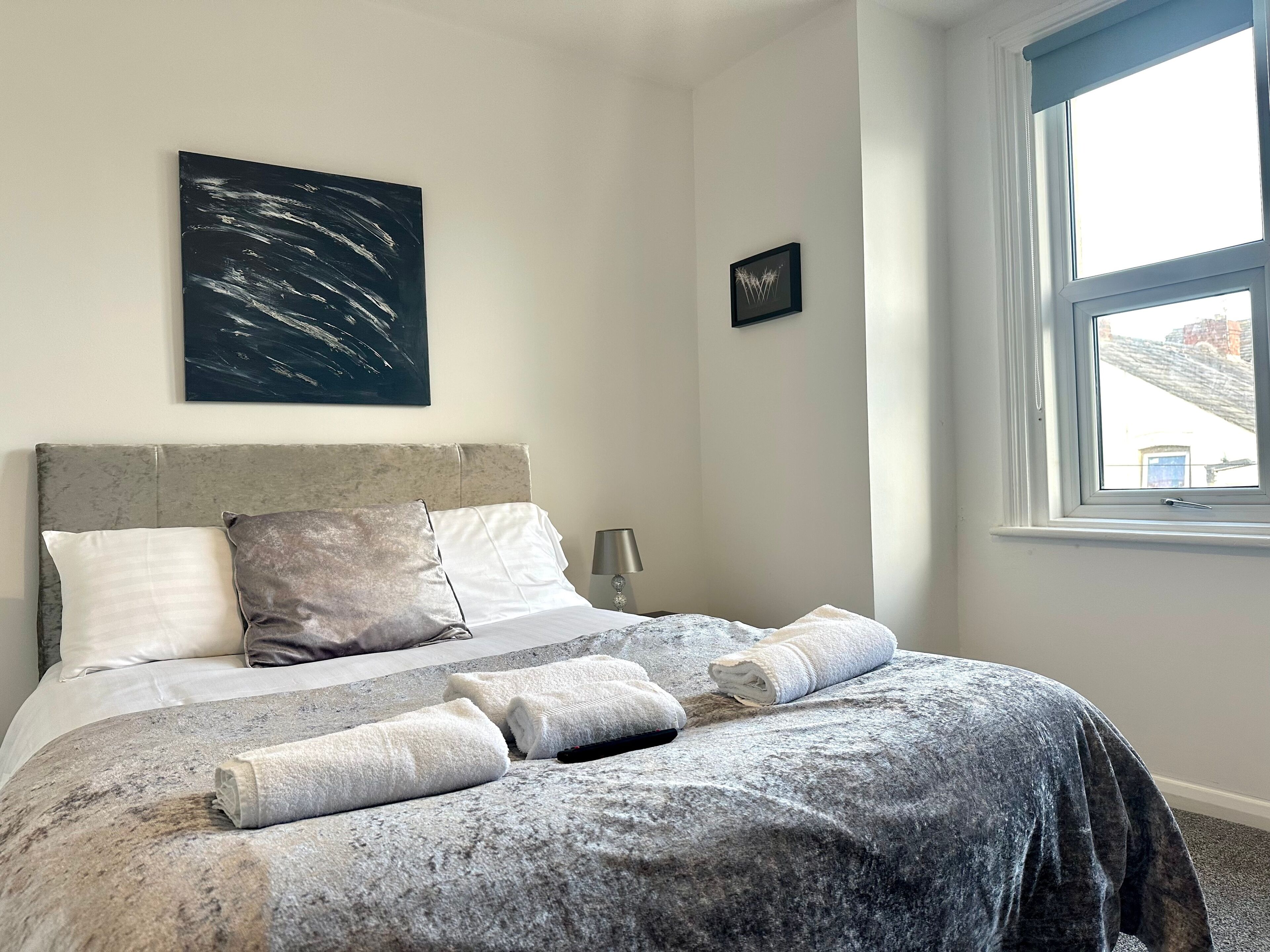 Ein ordentlich bezogenes Bett mit einer grau-weißen Bettdecke, zwei Kissen und aufgerollten Handtüchern.