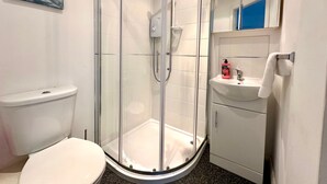 A modern bathroom with a glass-enclosed shower, a white toilet, a sink with a mirror, and a small towel rack.
