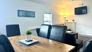 A conference room with a wooden table, black leather chairs, a potted plant, a flat-screen TV, and a chandelier.