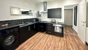 A modern kitchen with black cabinetry, a built-in washing machine, and a wooden floor. - Sienna Ground Floor 2Bed with Garden (Blackpool)