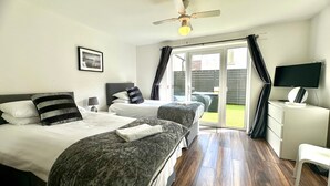 A hotel room with two beds, a ceiling fan, a TV, and a sliding glass door to the outside. - Sienna Ground Floor 2Bed with Garden (Blackpool)
