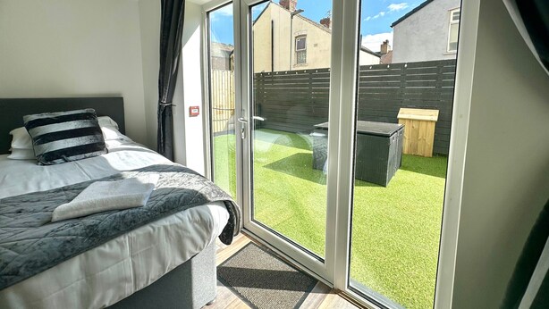 A bedroom with a bed, a window, and a view of a backyard. - Sienna Ground Floor 2Bed with Garden (Blackpool)