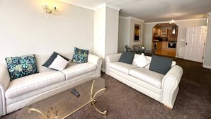 Ein Wohnzimmer mit zwei weißen Sofas, einem Couchtisch und einer Küche im Hintergrund.
