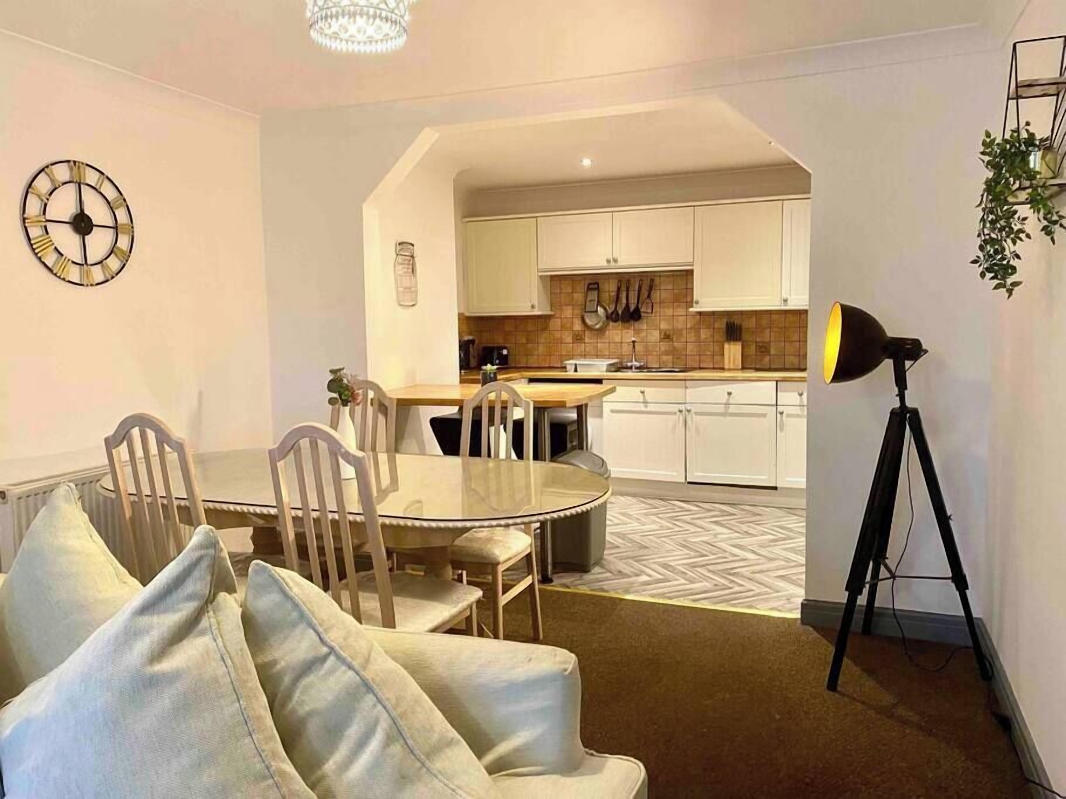A modern kitchen with white cabinets, a dining area with a round table and chairs, and a tripod-mounted lamp.