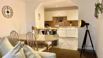 A modern kitchen with white cabinets, a dining area with a round table and chairs, and a tripod-mounted lamp.
