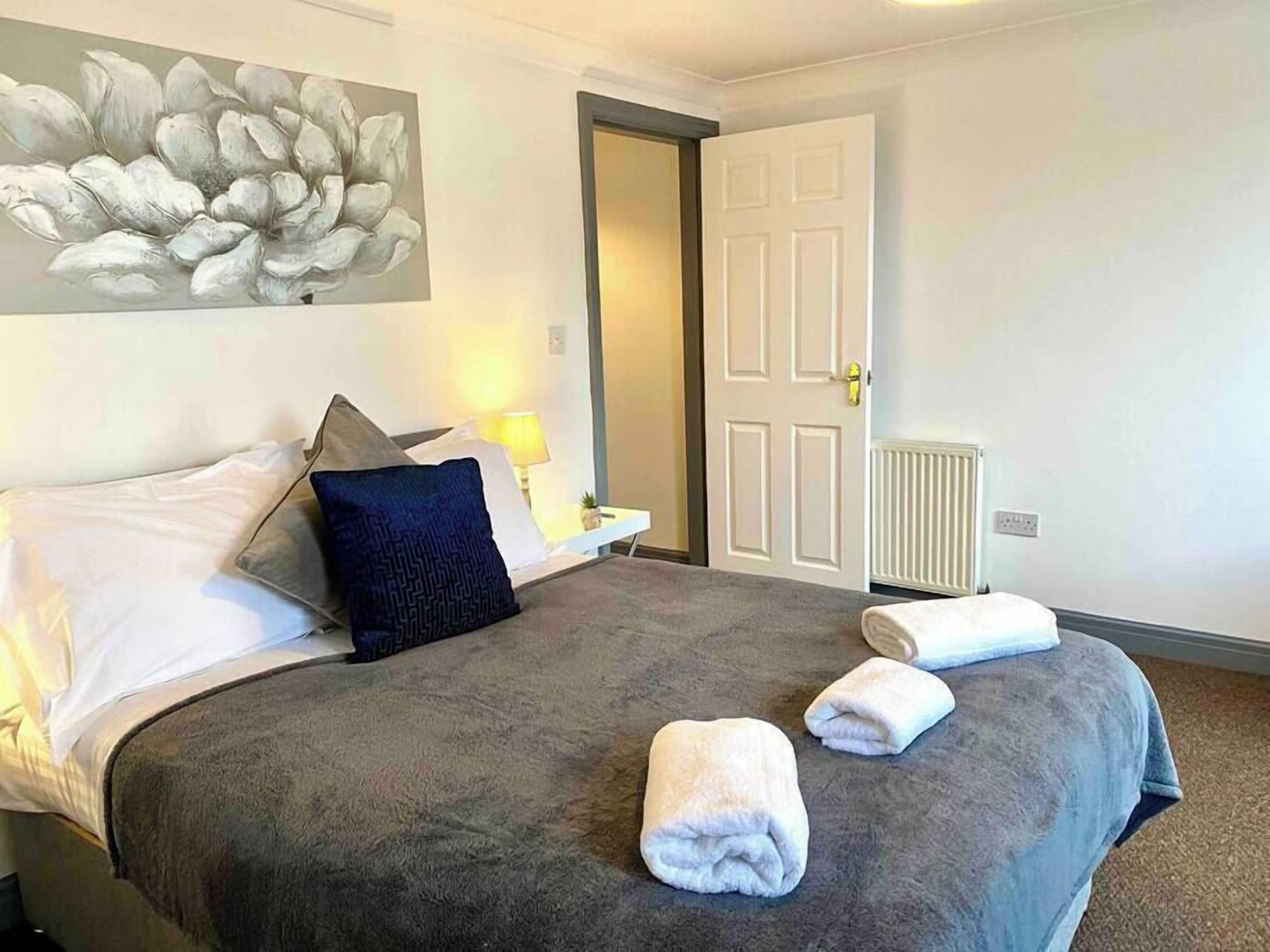 A hotel room with a large bed, a nightstand, a lamp, a door, and a radiator.