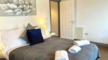 A hotel room with a large bed, a nightstand, a lamp, a door, and a radiator.
