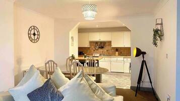 A modern living room with a sofa, a dining table, and a kitchen in the background.
