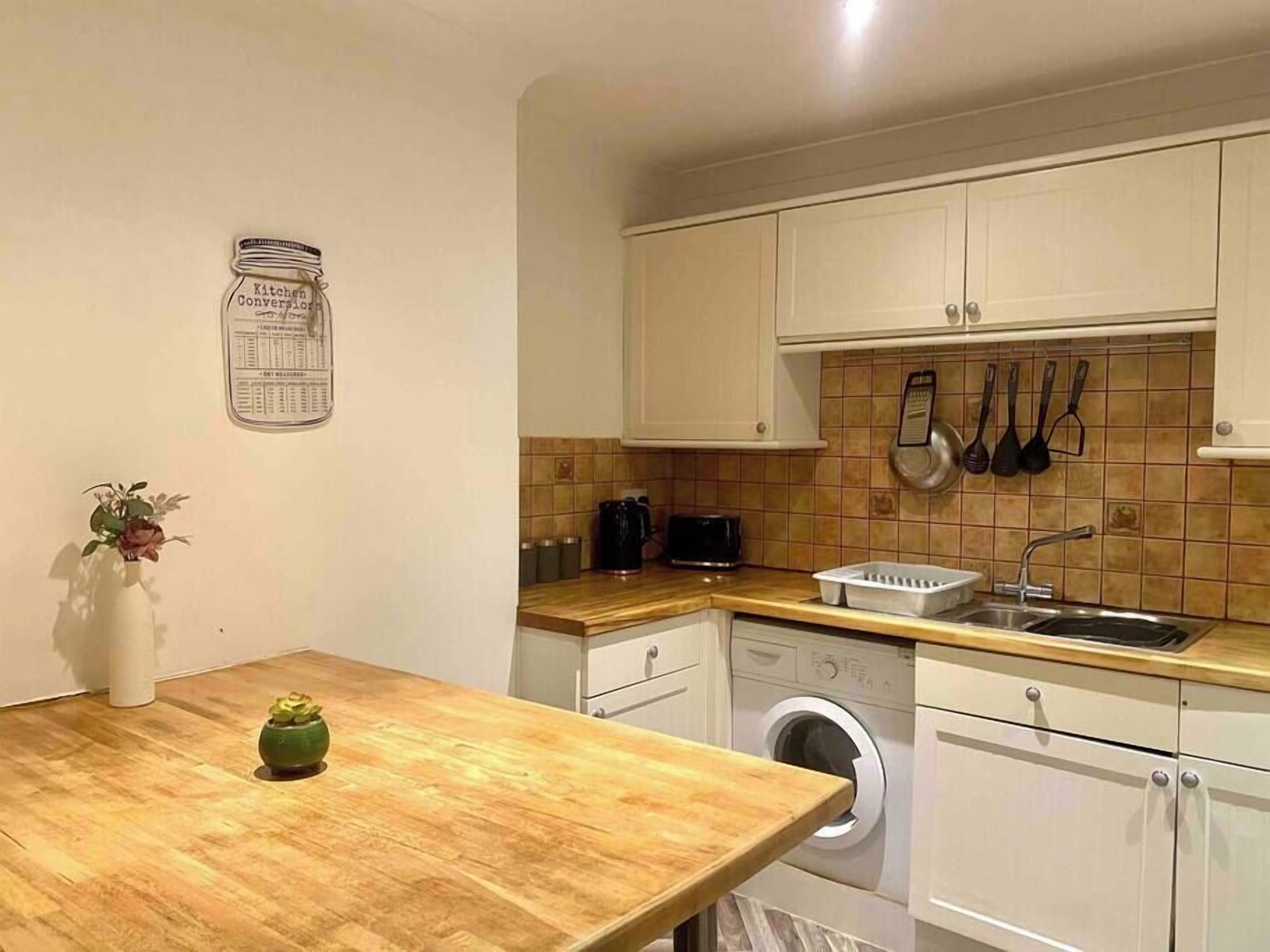 A compact kitchen with white cabinets, a wooden countertop, a washing machine, and a small potted plant.