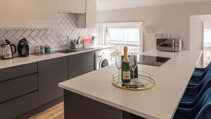 Une cuisine moderne avec un îlot central, un four à micro-ondes et un grille-pain. Une bouteille de champagne et un verre sont posés sur l’îlot.