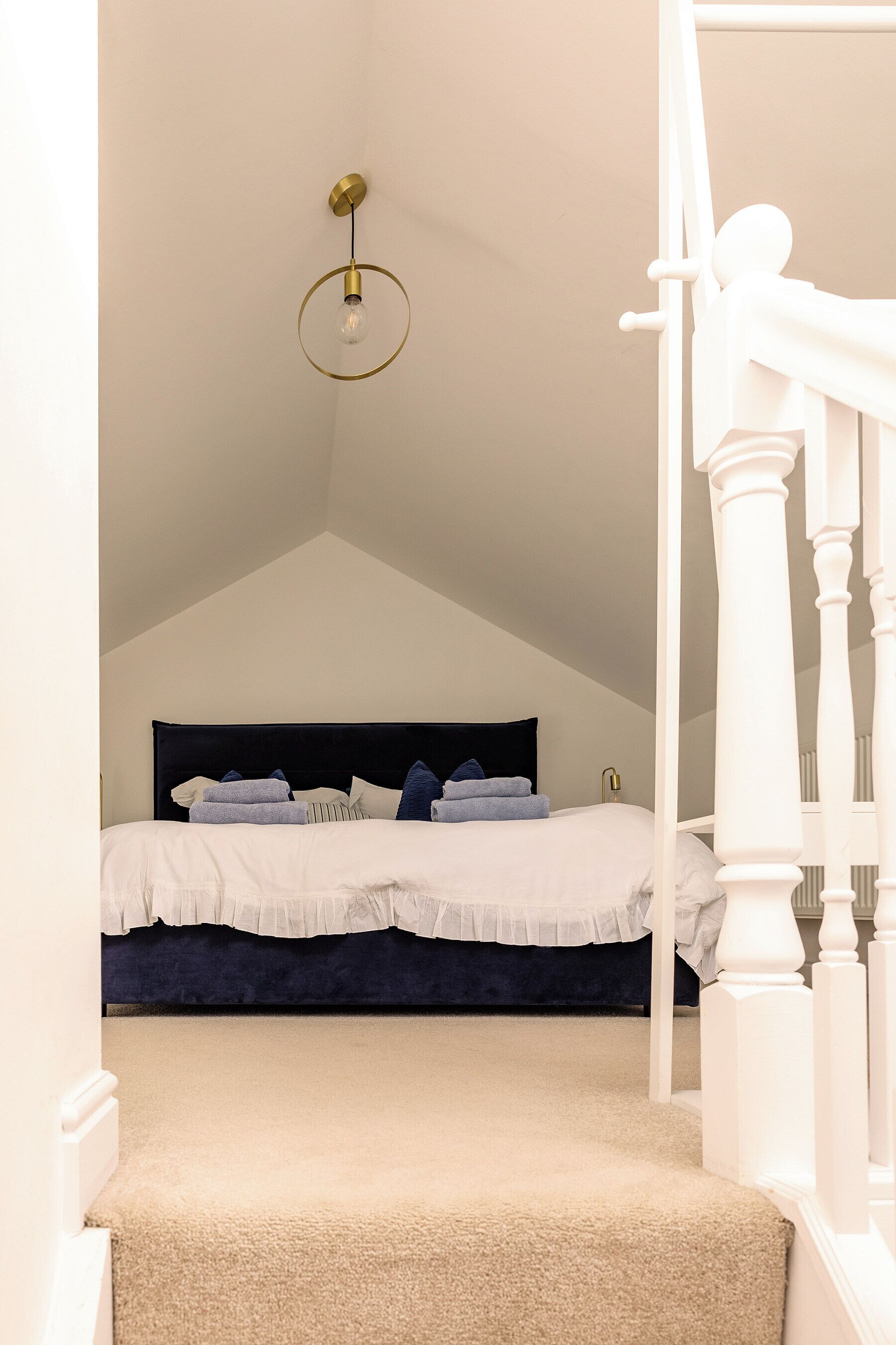 Ein Schlafzimmer mit einem weißen Bett, einem dunklen Kopfteil und einer weißen Treppe.