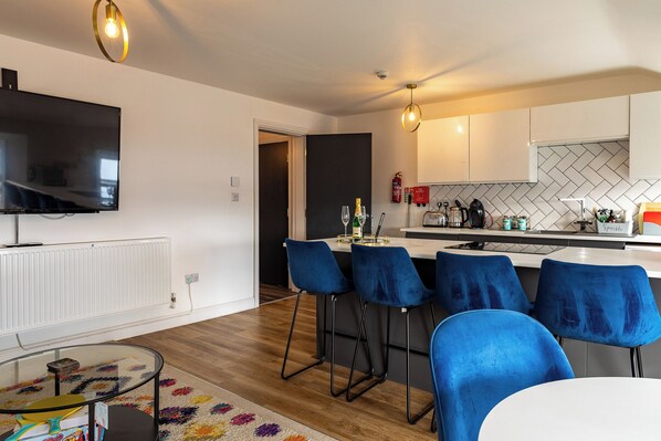 A modern kitchen with white cabinets, a black countertop, and a bar area with blue chairs.